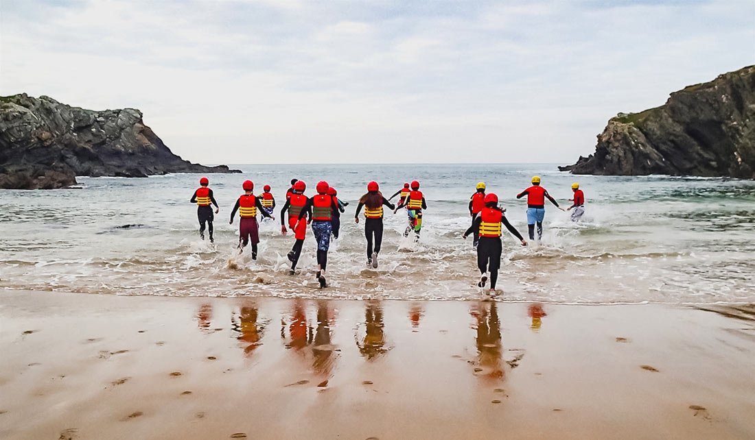 Large Coasteering group run into the sea at Porth Dafarch to acclimatize to the conditions