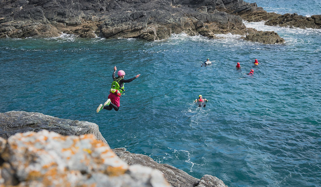 Man with pink helmet performs an epic Coasteering cliff jump into the sea below